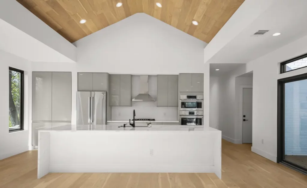 A custom luxury kitchen. White walls and counters with a light wood floor and ceiling.