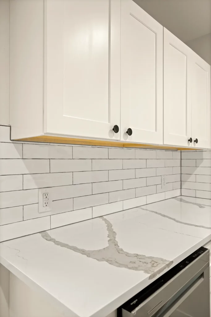 A kitchen marble countertop with white tile backsplash and white cabinets.