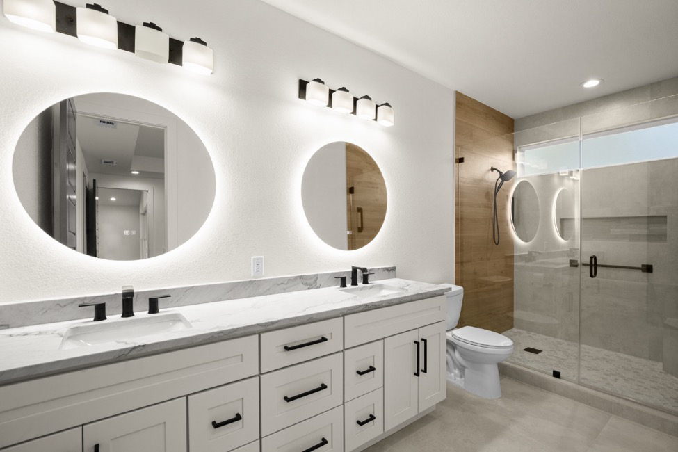 A remodeled bathroom with marble countertops, white walls, and dark fixtures and hardware, showing one of the latest bathroom makeover trends