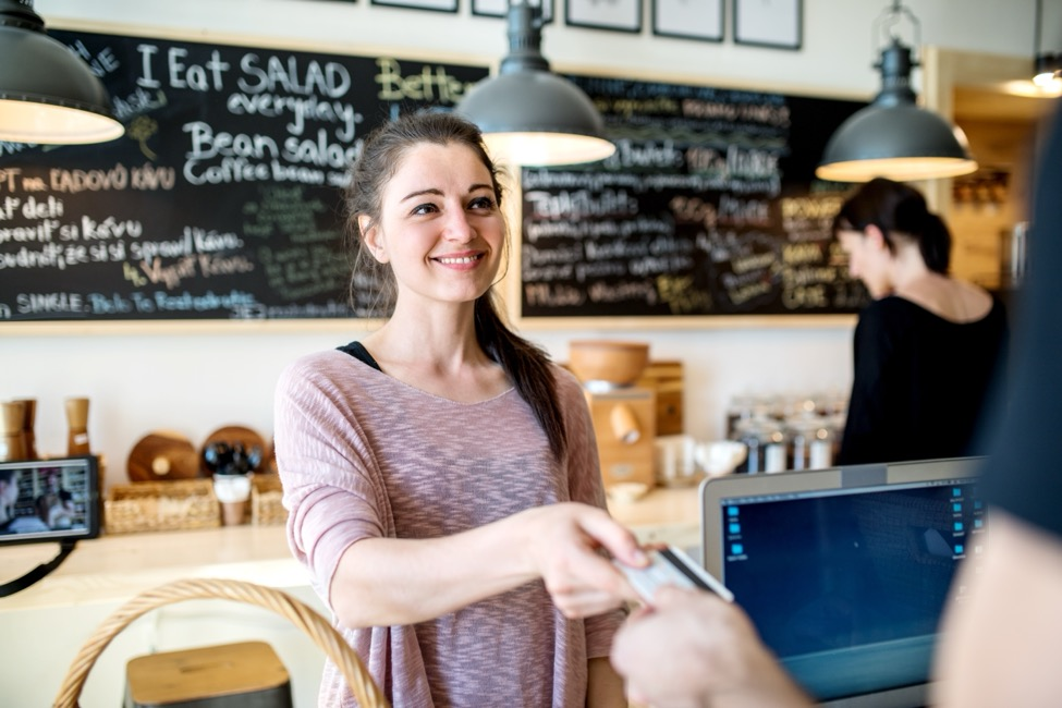 a female worker at a local deli takes a customer’s credit card