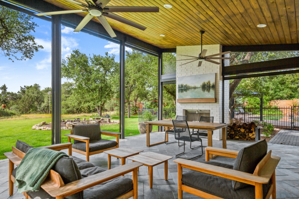 An outdoor room addition with a paver floor, wood ceiling, ceiling fans, and teak furniture.