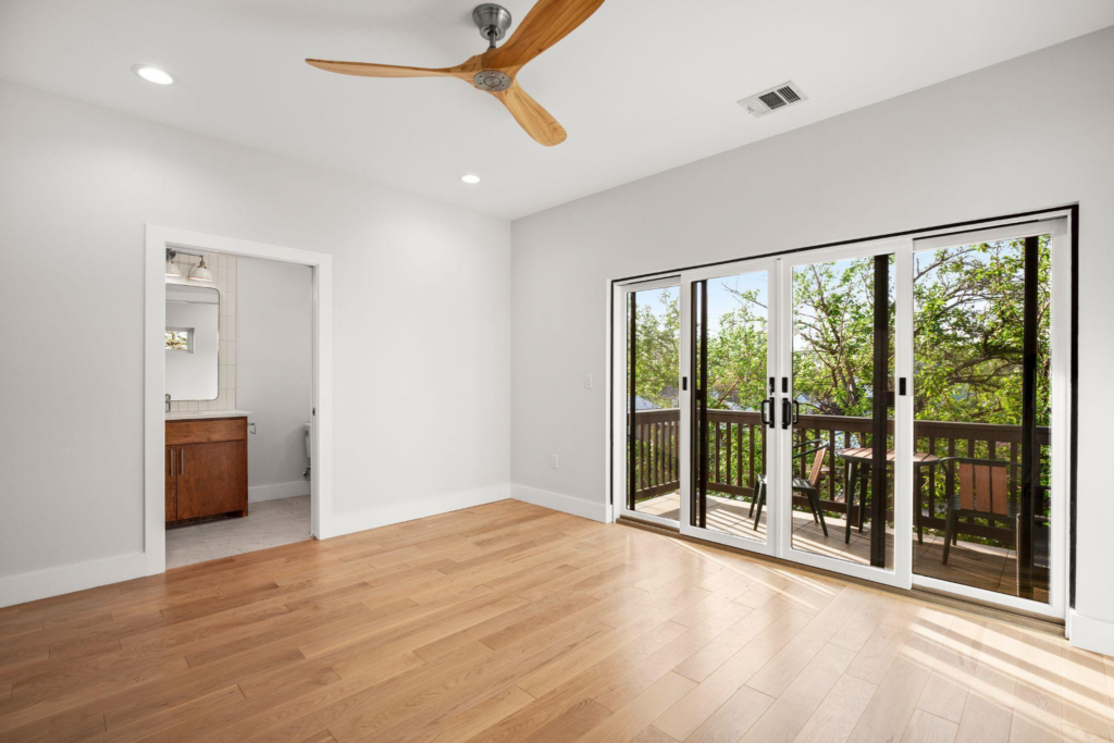 A room with a window, attached balcony, attached bathroom, and a fan 