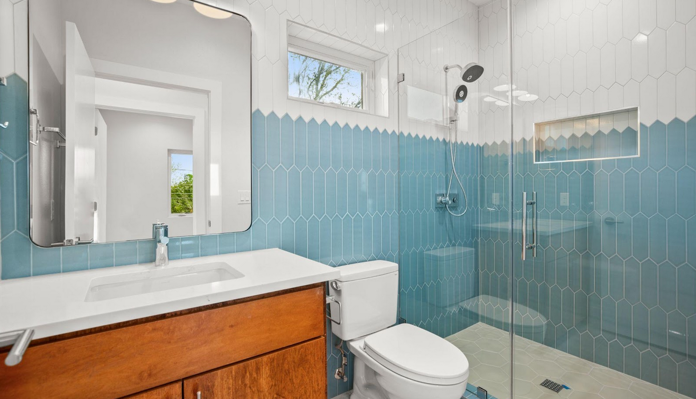 A bathroom renovation with a sink, toilet, mirror, and shower, and blue walls