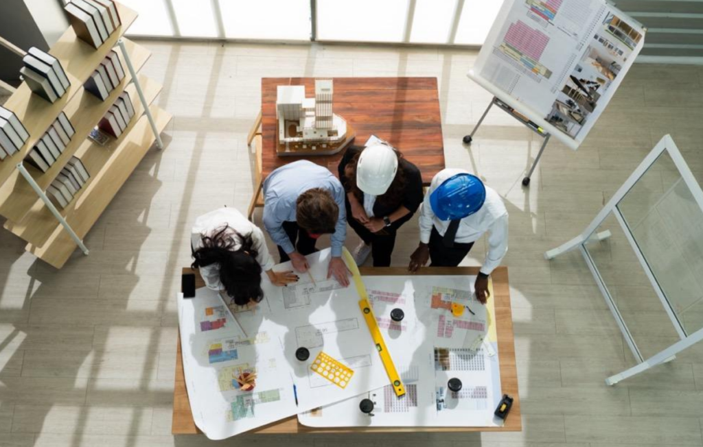 four commercial construction team members gather around a table to discuss blueprints for an office buildout project