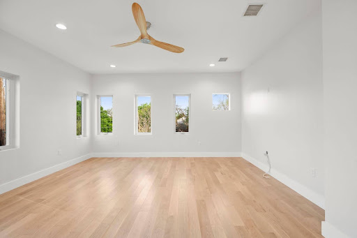 An empty home addition with a wooden floor, windows, and a fan