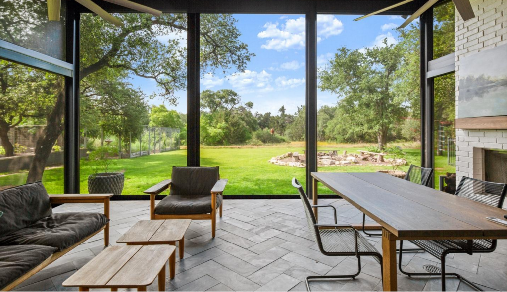 An outdoor living space room addition with teak sofas and chairs, a long dinner table and a fireplace