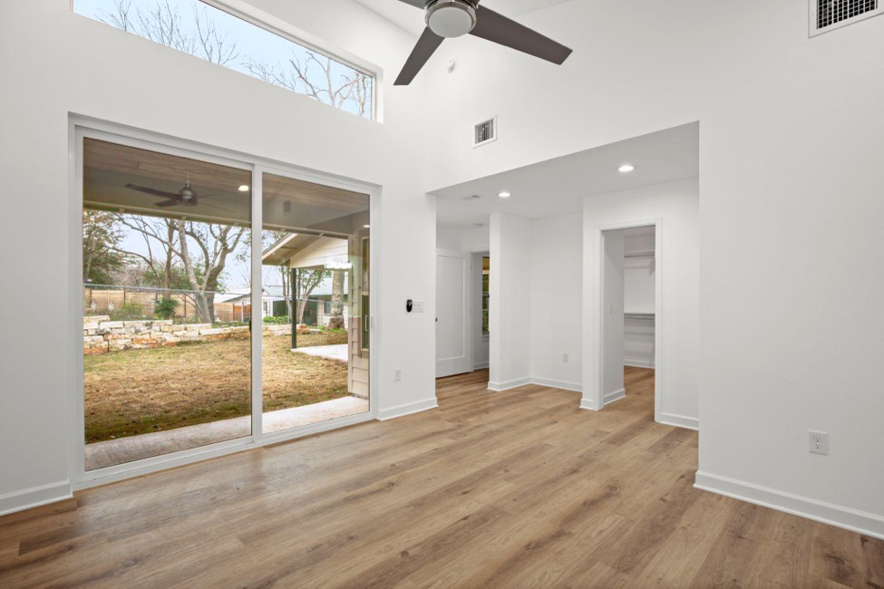 A room inside a luxury house with a fan, a large window, wooden floors, and multiple doorways