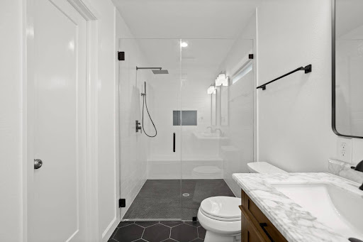 A bathroom with a sink, toilet, mirror, and shower, and white walls 