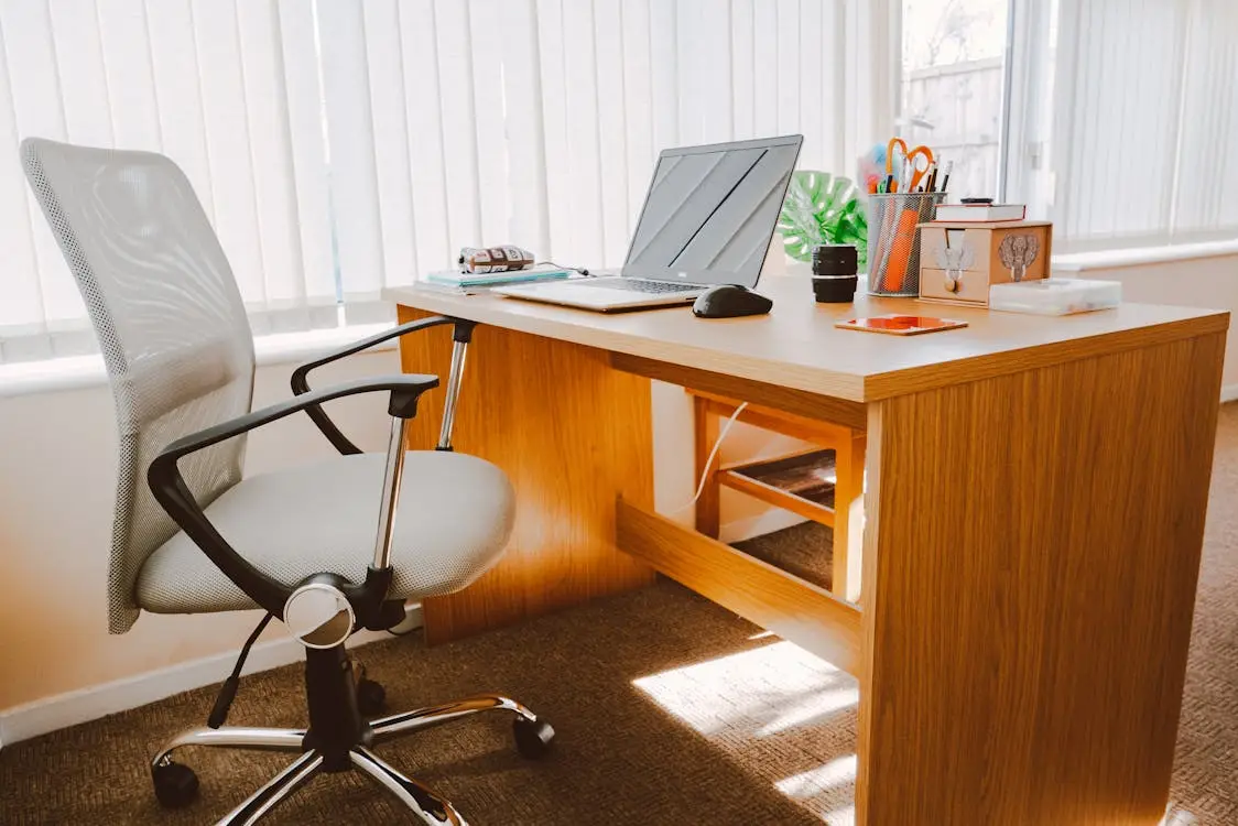 A laptop on a wooden desk alongside a chair in a small office