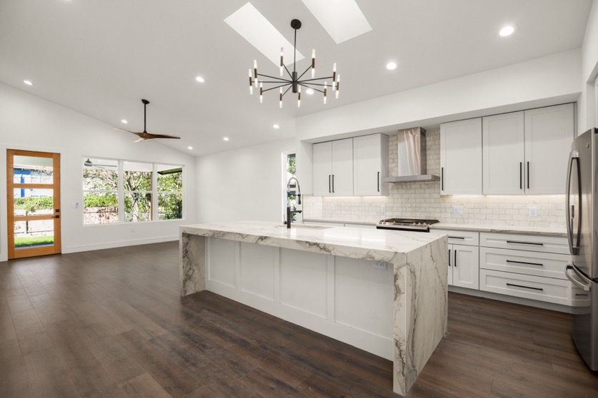 A luxury kitchen with white cabinets, stainless steel appliances, and dark-finish fixtures in a large space.