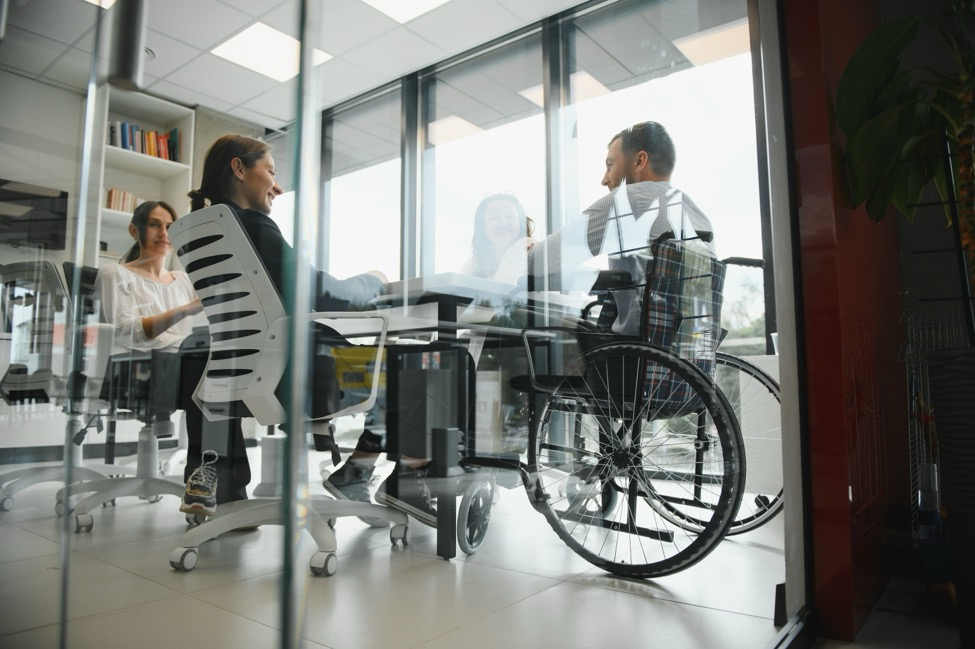 A man in a wheelchair sits at a conference room table with colleagues.