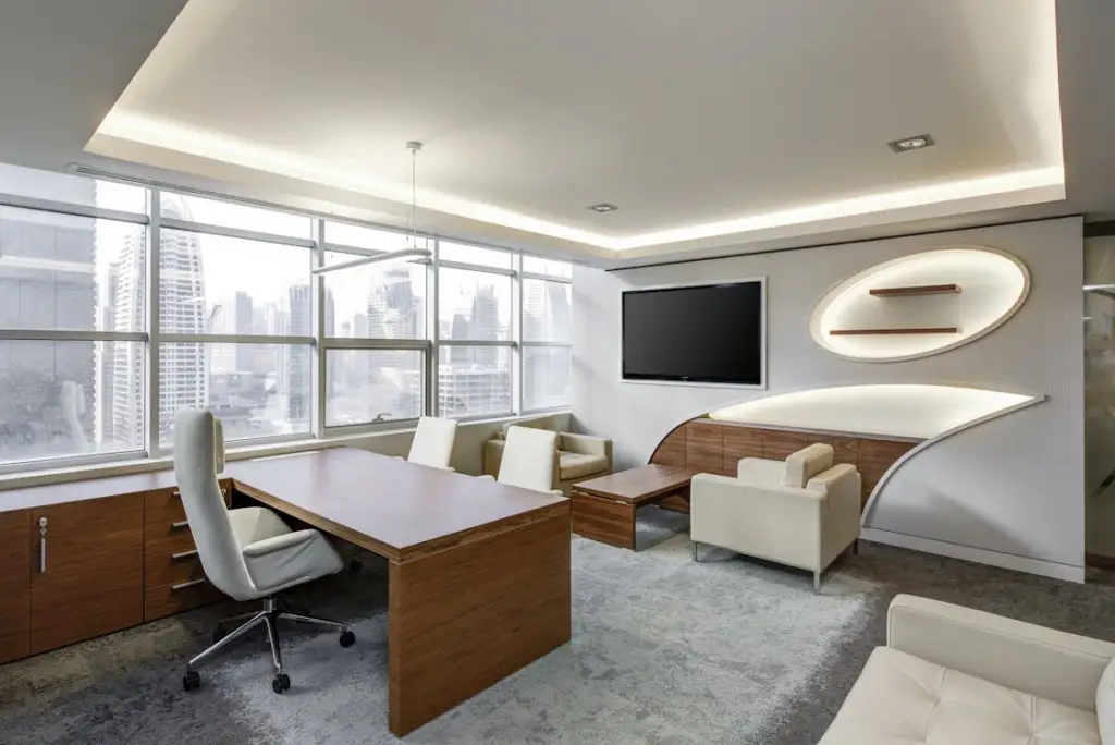 An office room with a couch, table, chairs, armchairs, a TV screen, and mirrors on the wall