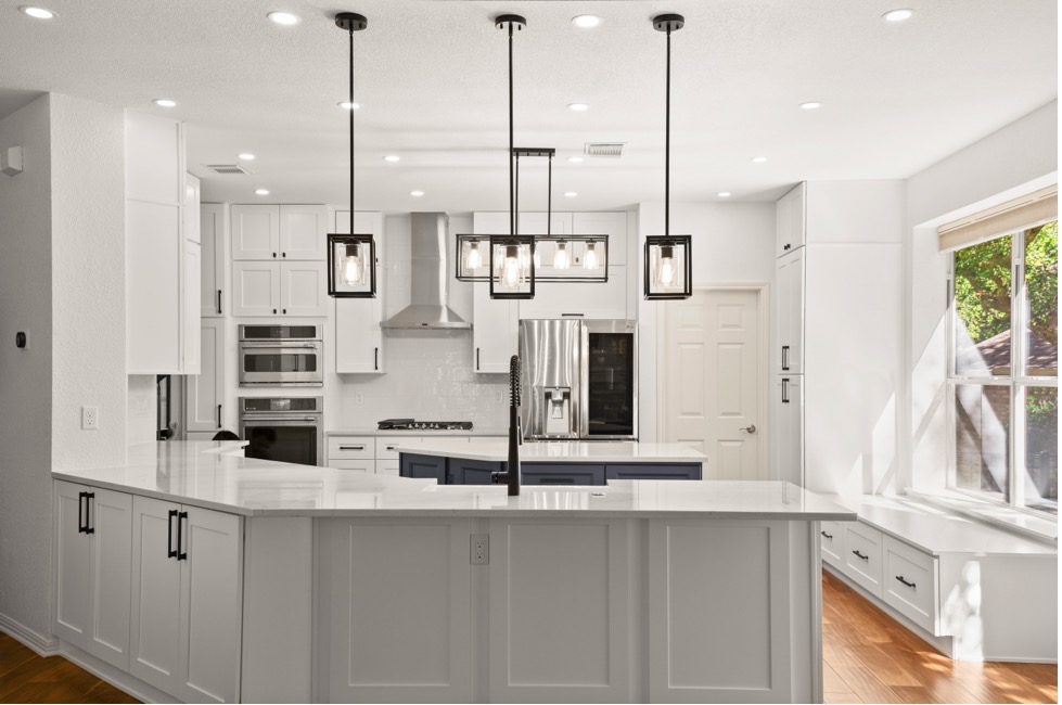 A luxury kitchen with white walls and countertops, a dark cabinet island, a brown wood floor, and stainless appliances.