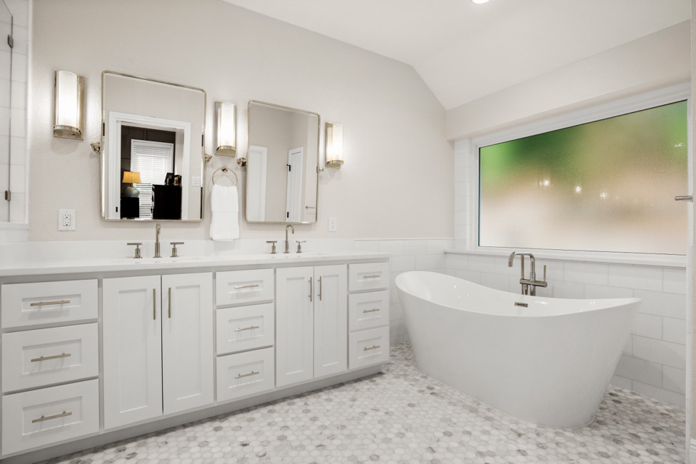 A white bathroom remodel with a sink, mirror, spa-style tub, and picture window