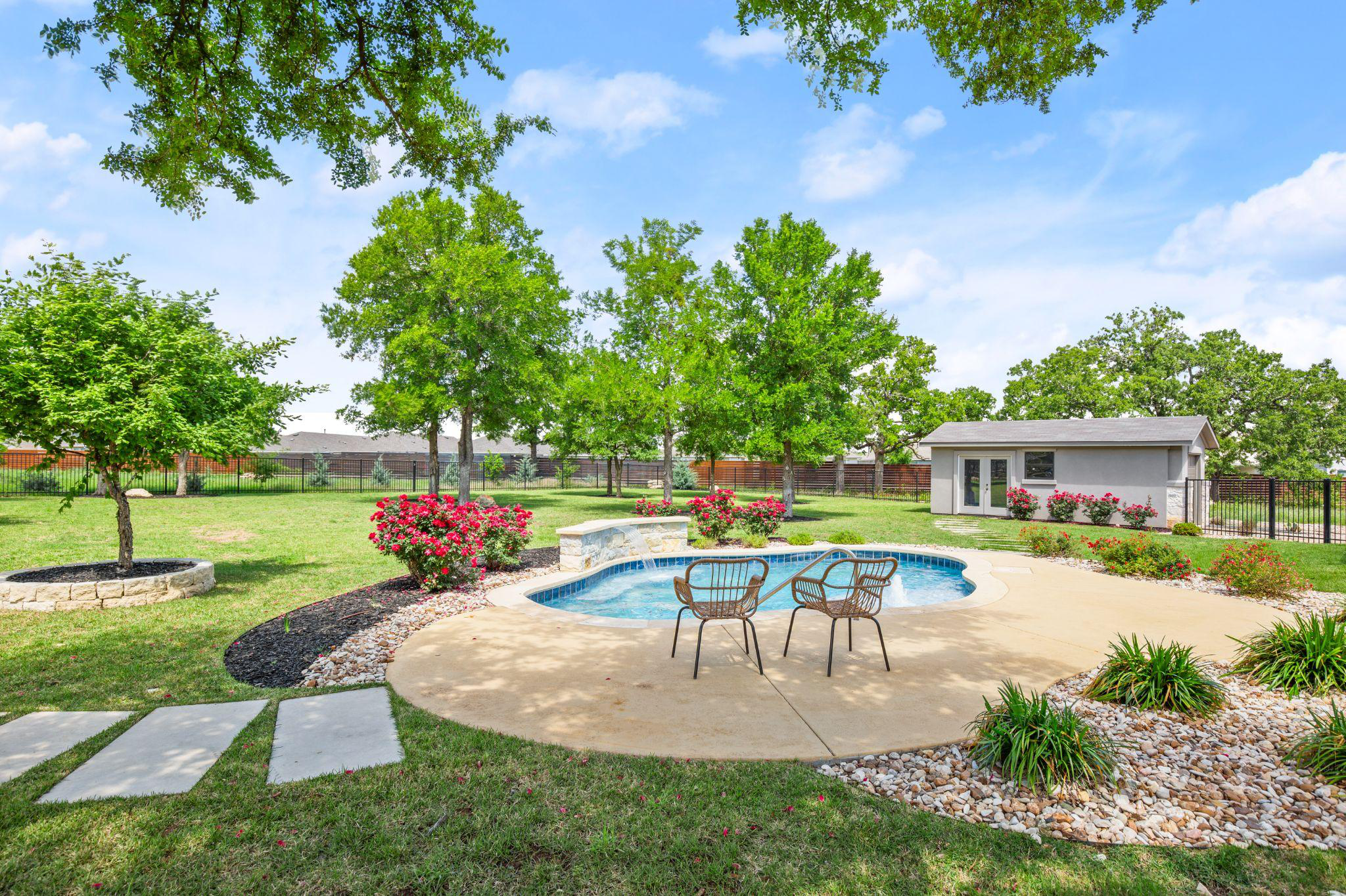 A pool surrounded by chairs, grass, flowers, and plants in a home’s backyard