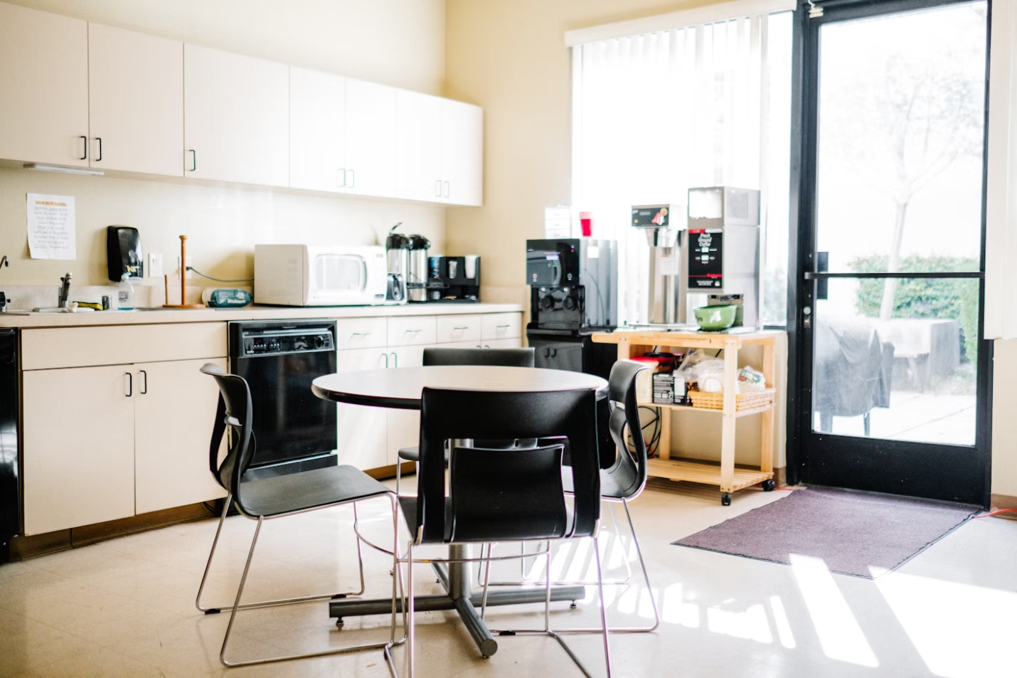 An office kitchen with a table, chairs, appliances, shelves, and a door