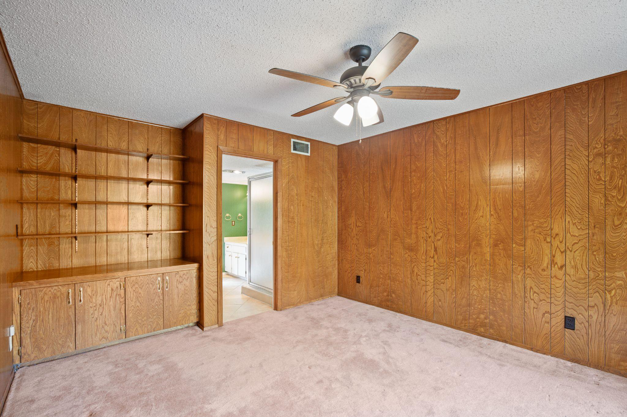 A room with a doorway, wooden walls, shelves, and cabinets