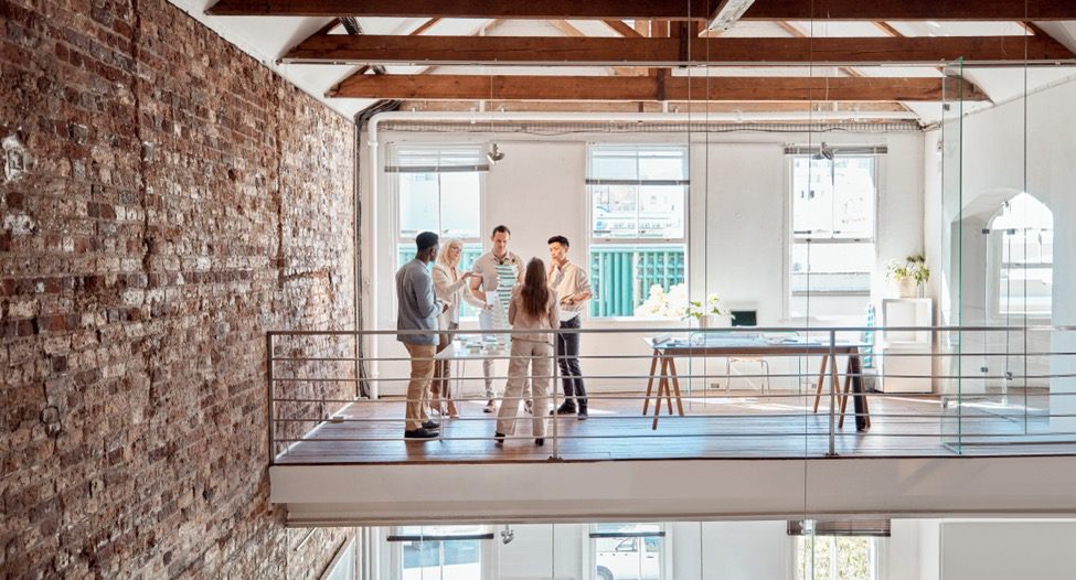 The interior of a commercial office space with a balcony, exposed brick, and wood ceiling beams