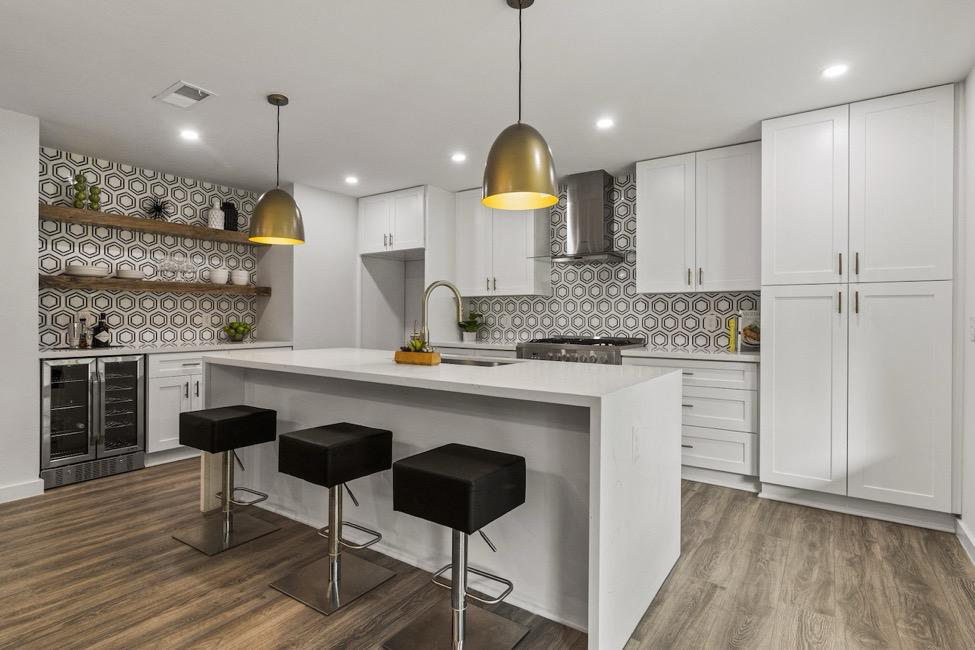 A kitchen with an island, stools, shelves, and storage cabinets