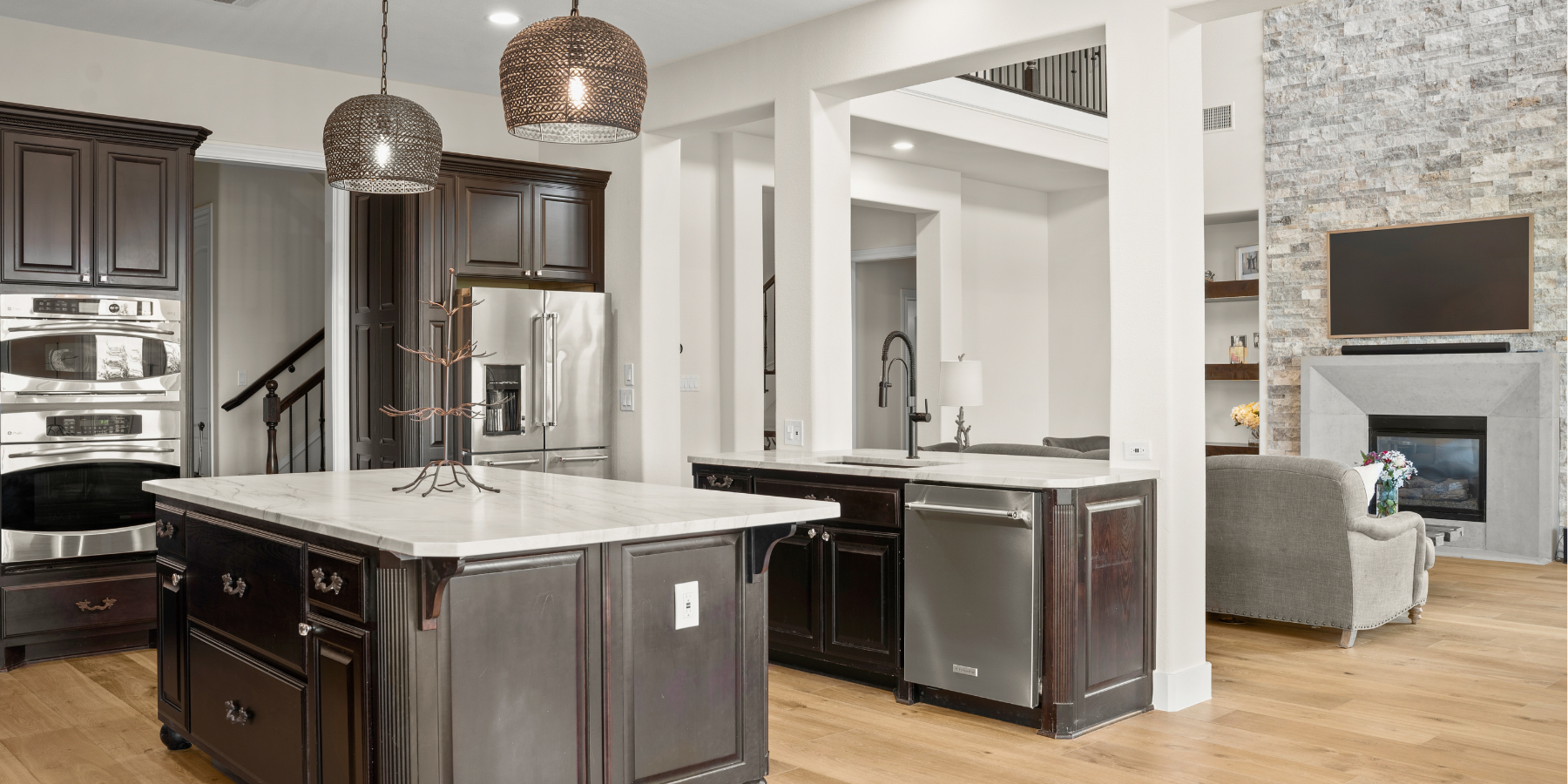 Open kitchen and living space with dark wood cabinets, marble island, stainless appliances, and stone fireplace