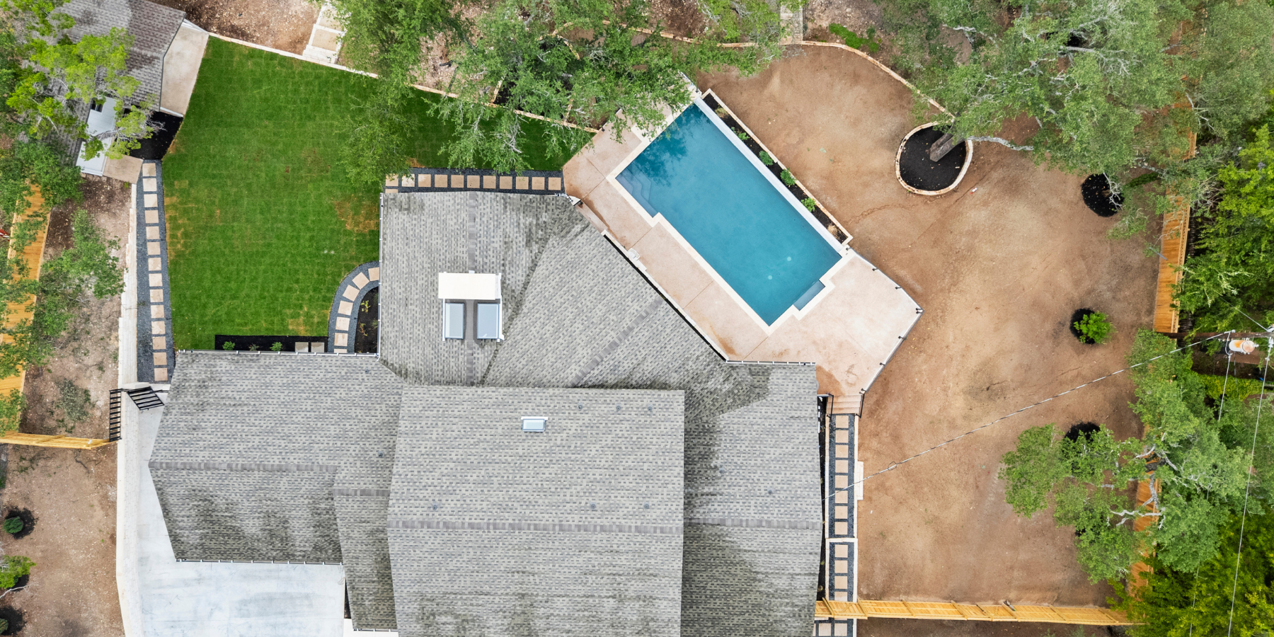 Aerial view of Freccia Group home with gray roof, rectangular pool, fenced yard, and surrounding trees