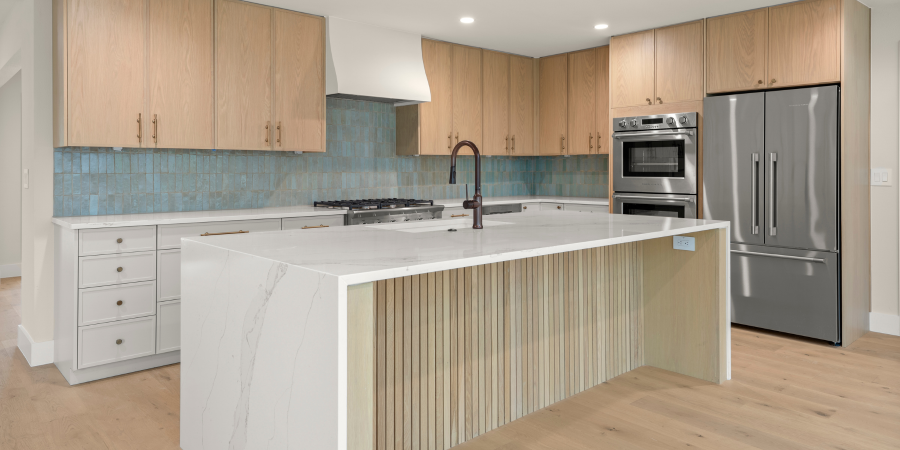 Modern kitchen with wood cabinets, blue tile backsplash, marble island, and stainless steel appliances