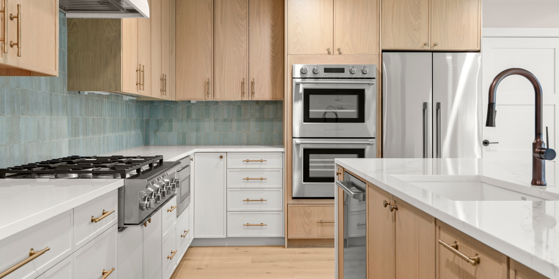 Modern kitchen with wood and white cabinets, marble countertops, double ovens, and blue tile backsplash