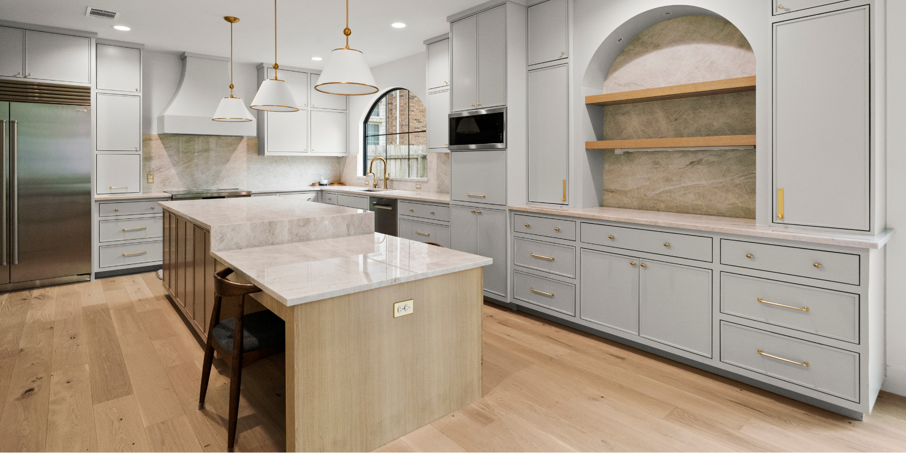 Luxury kitchen with marble countertops, light grey cabinets, gold hardware, and a large center island