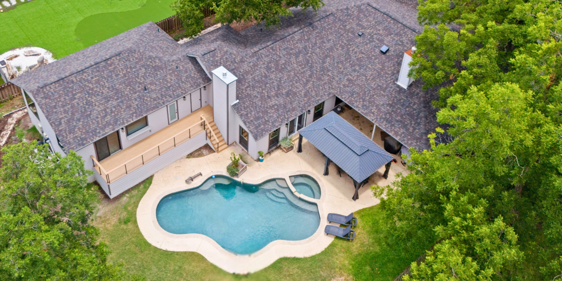 Aerial view of home with curved swimming pool, patio pavilion, and surrounding trees