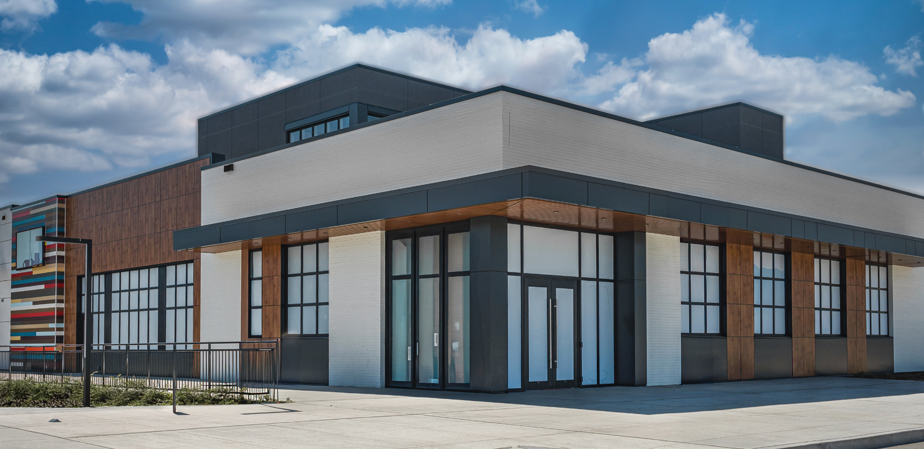 Modern commercial building exterior with large windows, clean lines, and wood accents under a blue sky
